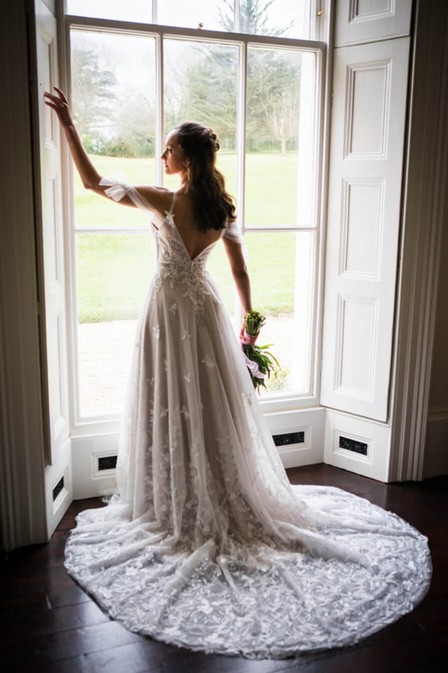 full back shot of bride standing by the window looking out, wedding dress back details of soft flowing dress