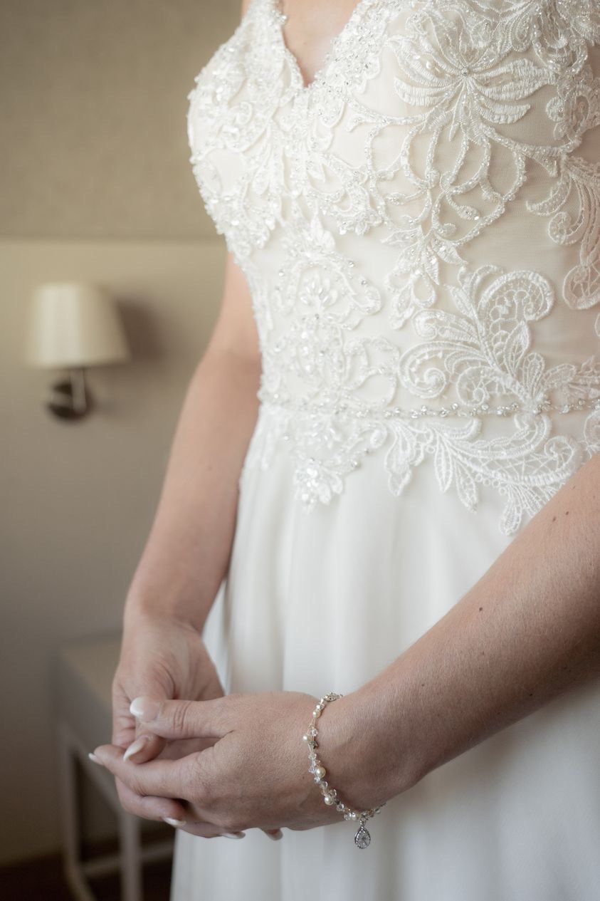 Wedding dress close up details of beaded lace and personal bridal bracelet