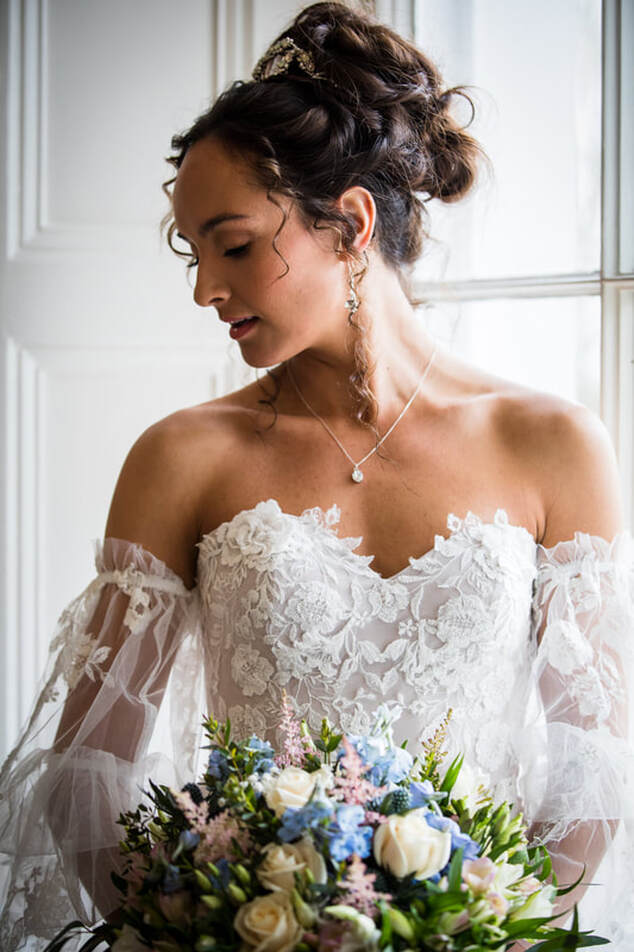 bride holding pale blue and pink bouquet, soft blush wedding dress and silver sparkly jewellery, hair up