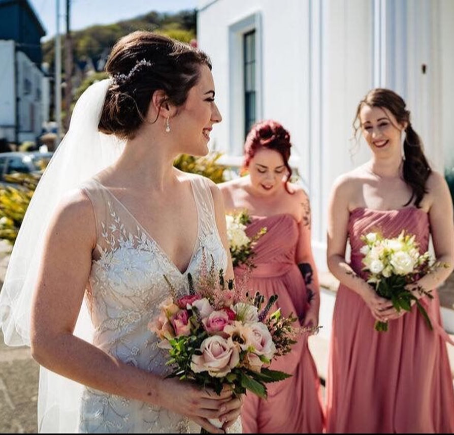 bride with beaded dress, rose gold wedding hairpiece and freshwater pearl drop earrings, pale pink bouquet and bridesmaids dressed in pink on the wy to the wedding on a sunny day