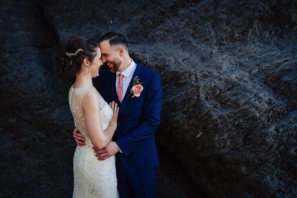Bride and groom tunnels beach by the rocks, rose gold hair vine and pink buttonhole