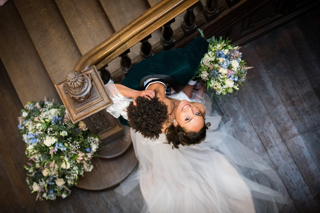 bride and groom on the stairs looking up, manor house staircase with floral decorations